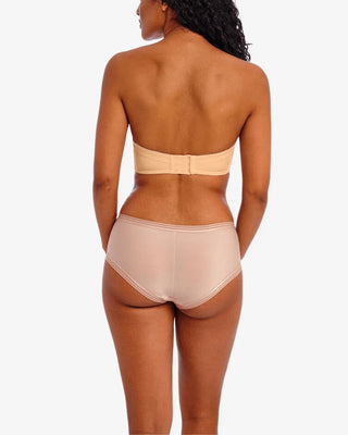 Modell sedd bakifrån bär en beigefärgad axelbandslös BH med hakknäppning samt beige transparent trosa med täckande baksida