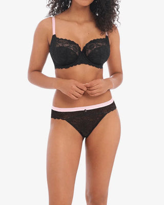 Modell bär Freya Offbeat bh och brazilian trosa – svart spets med blushrosa midjeband
