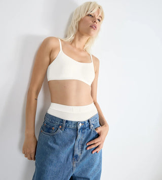“Modell bär Sloggi GO Daily Cotton BH-Top i blåa jeans – bygelfri ekologisk bh med dubbla lager kupor och justerbara axelband för lätt stöd.”