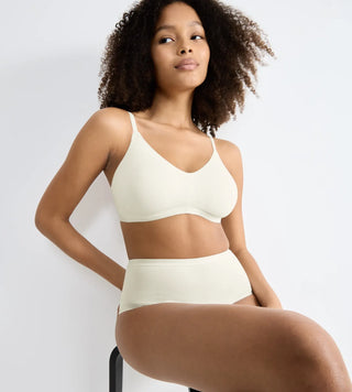 “Modell bär vit Sloggi GO Daily Cotton Soft Bra sittandes på en stol – mjuk bomulls-bh utan bygel med lätt stöd och justerbara axelband.”