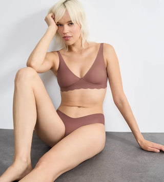 “Modell bär Sloggi Zero Microfibre Soft Bra i nyansen cacao sittandes mot en vägg – sömlös bh med medium stöd och justerbara axelband i hudnära ton.”